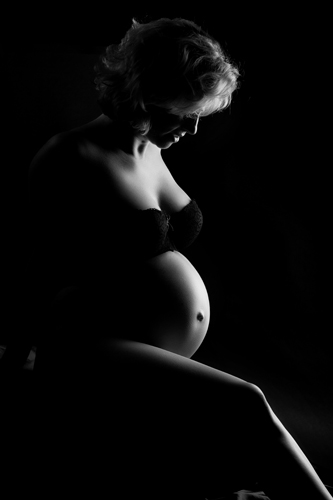 Fotografie Schwangerschaft Düsseldorf. Schwangere mit nacktem Babybauch tritt halb aus dem Dunkel. Sie sieht aus wie Marylin Monroe.