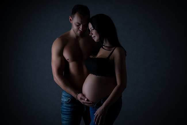 Babybauchfotografie Düsseldorf. Partner steht neben seiner schwangeren Frau und hät zärtlich ihren Schwangerschaftsbauch